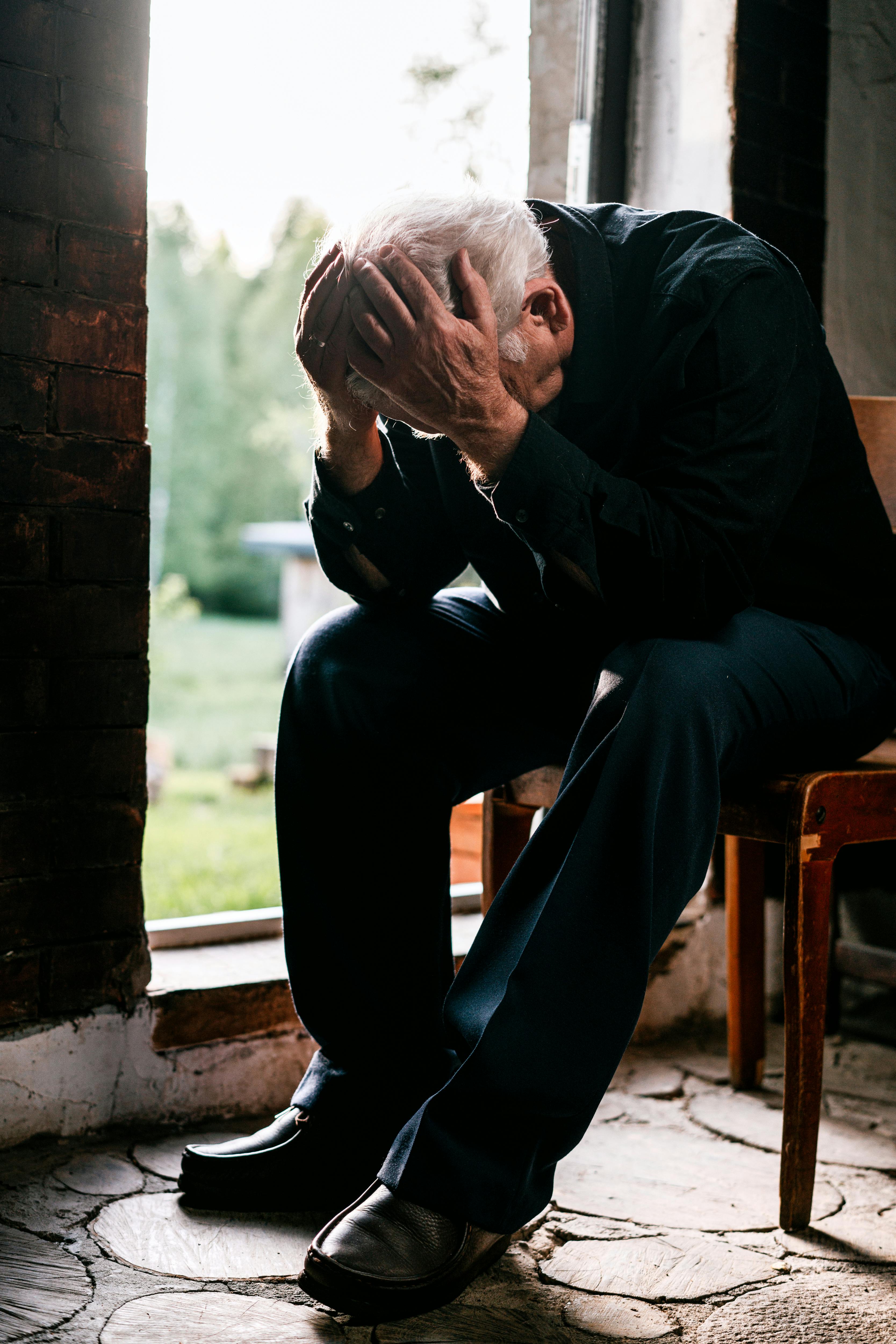 Older male sitting with face in palms and struggling