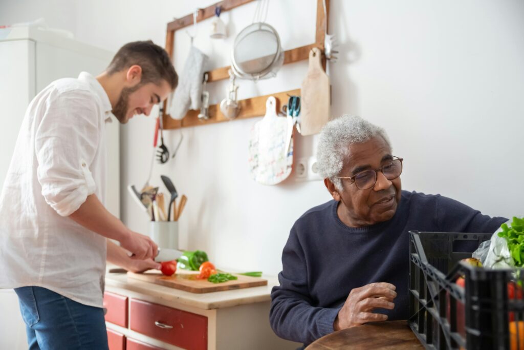 Man sorting vegetables, while younger man is cooking.